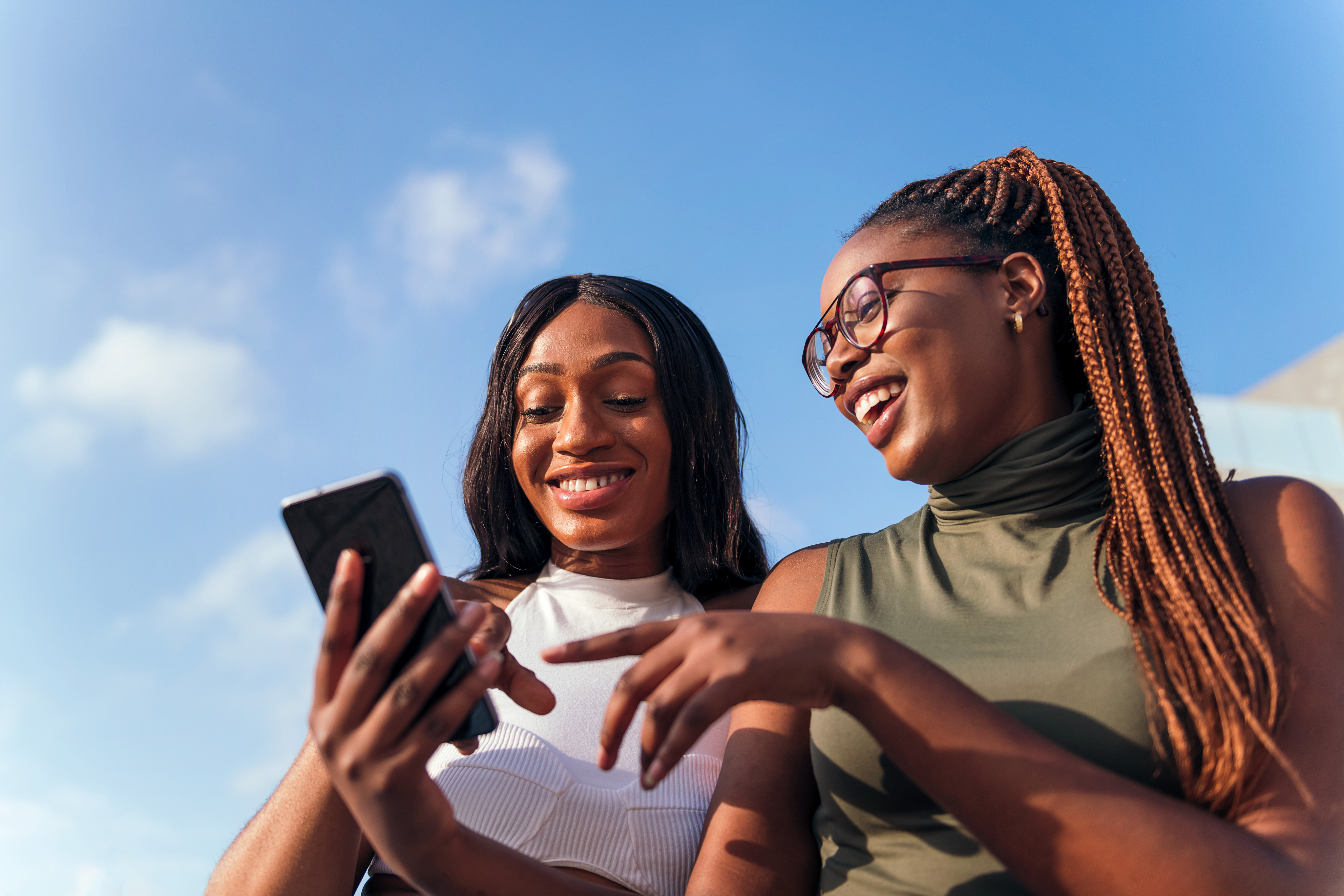 Deux femmes souriantes regardent un téléphone.