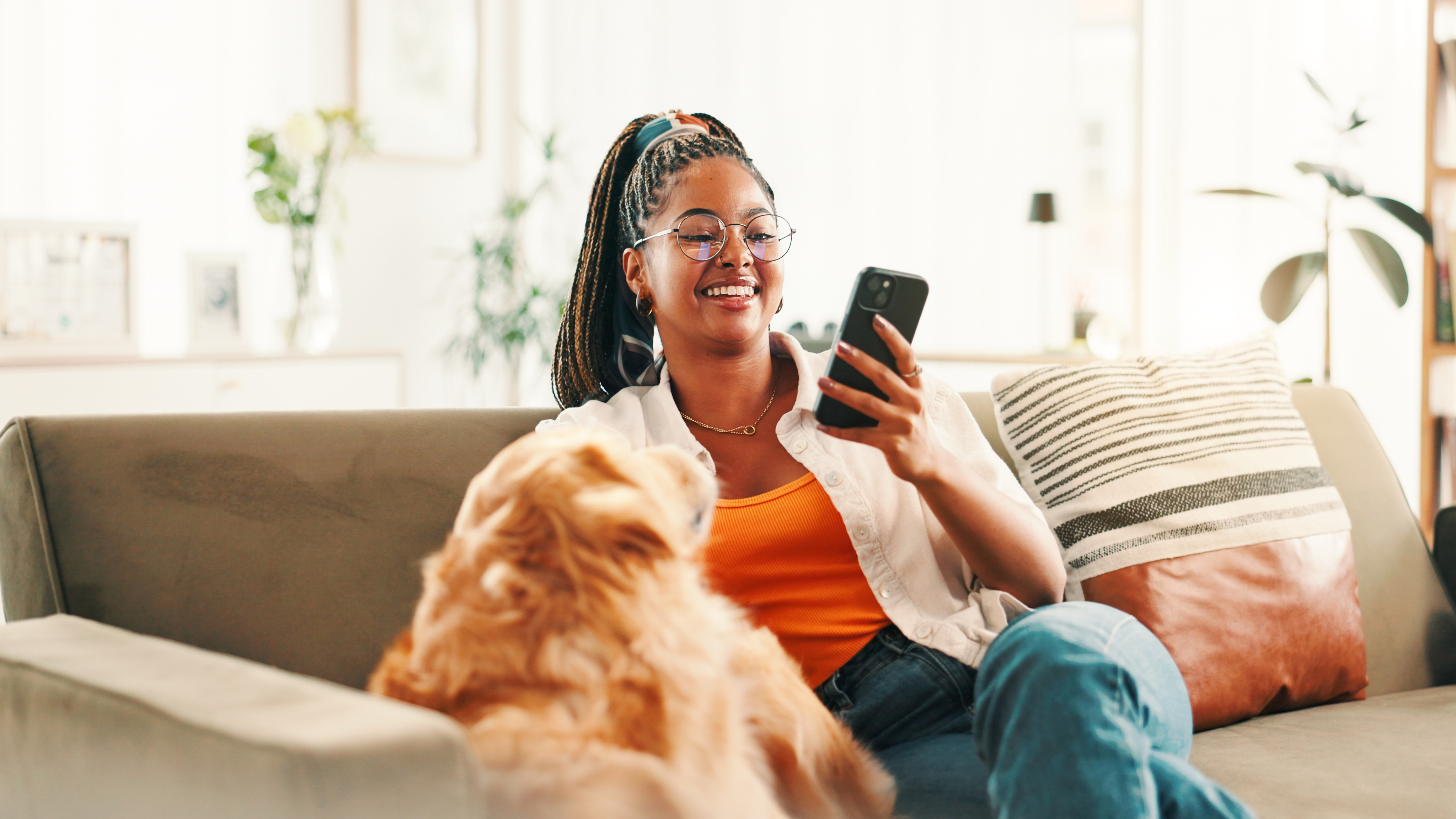 Une femme consulte son téléphone, assise sur un canapé avec son chien.