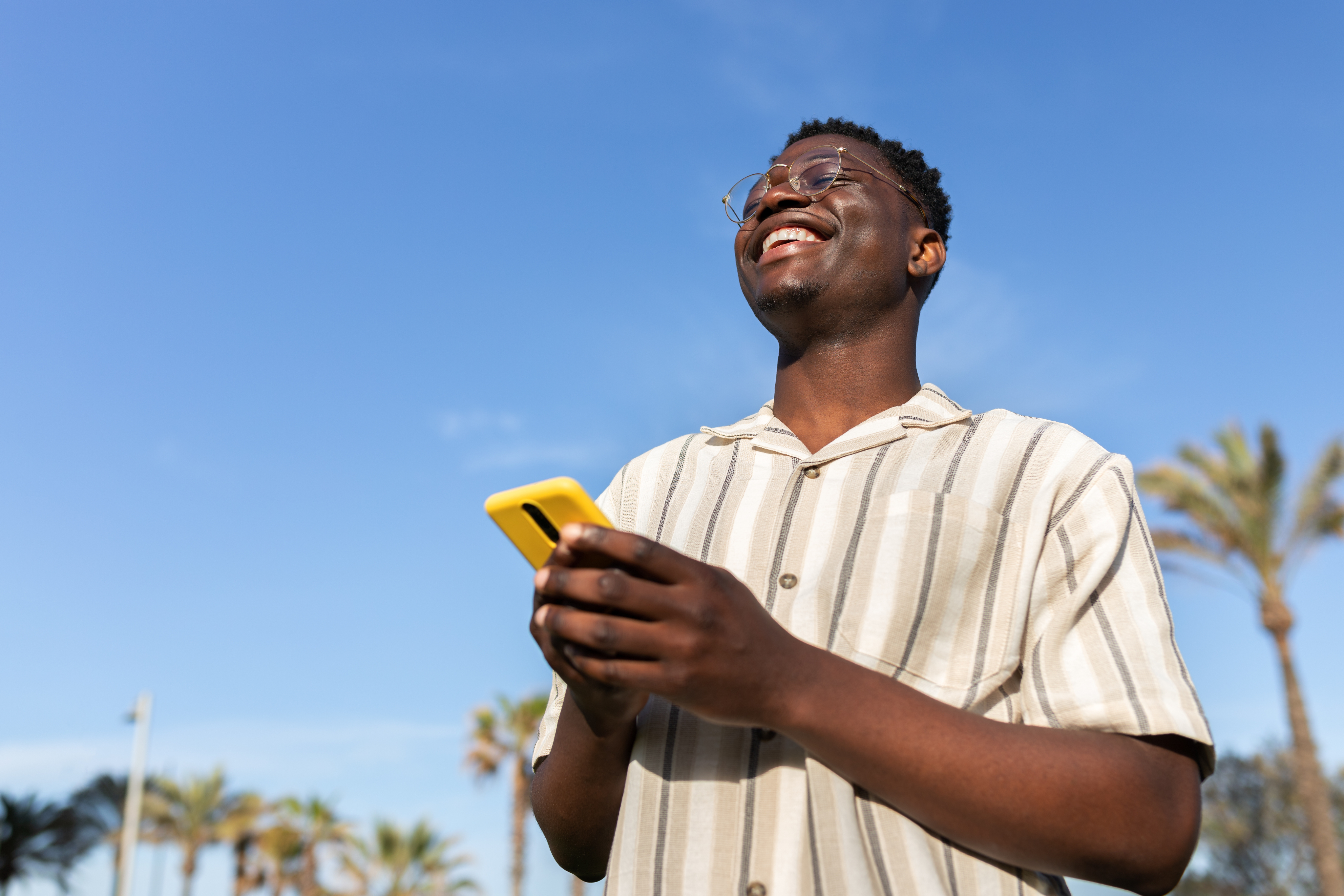 Un homme portant des lunettes consulte son téléphone à l’extérieur.