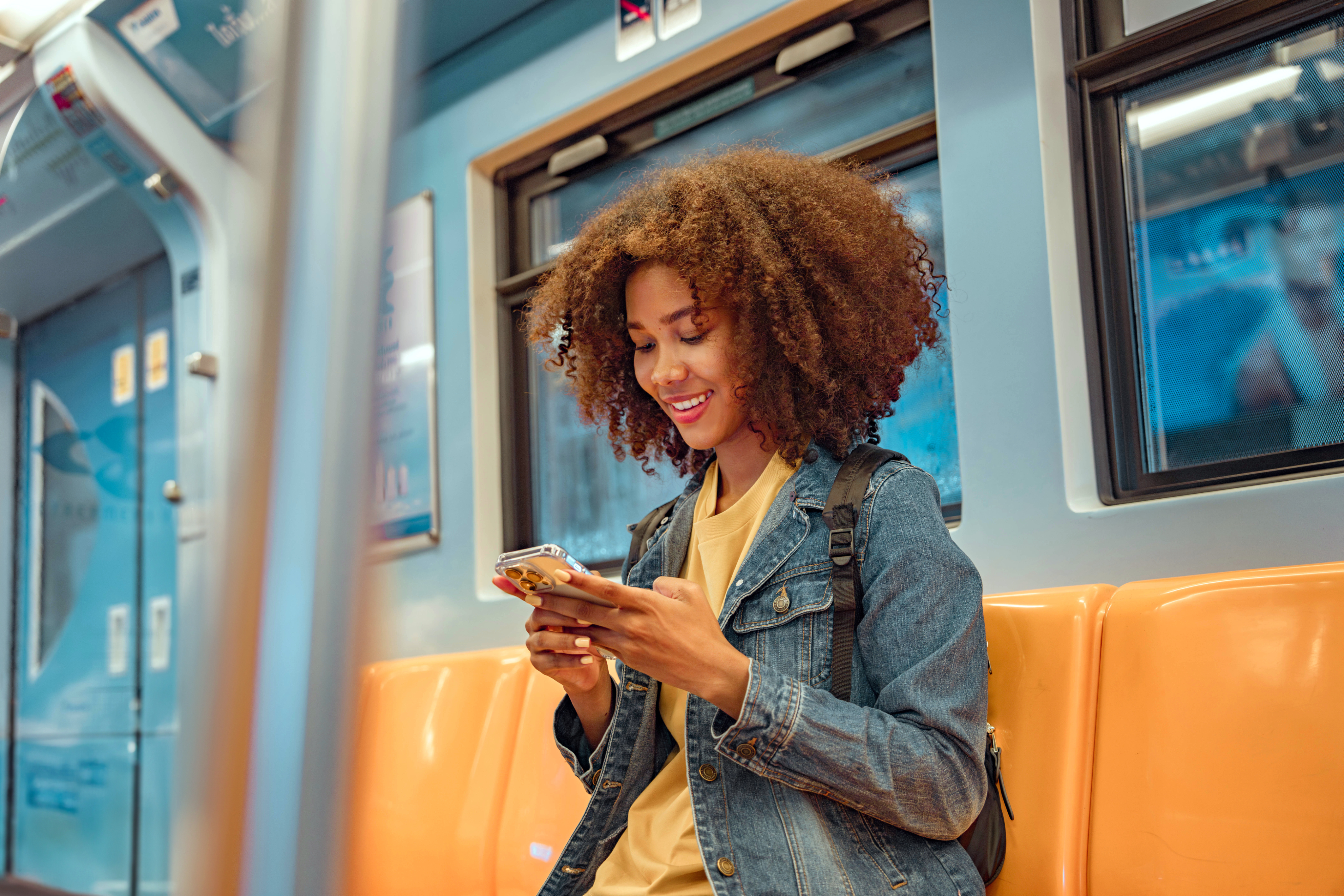 Une femme aux cheveux bouclés utilise son téléphone dans le métro.